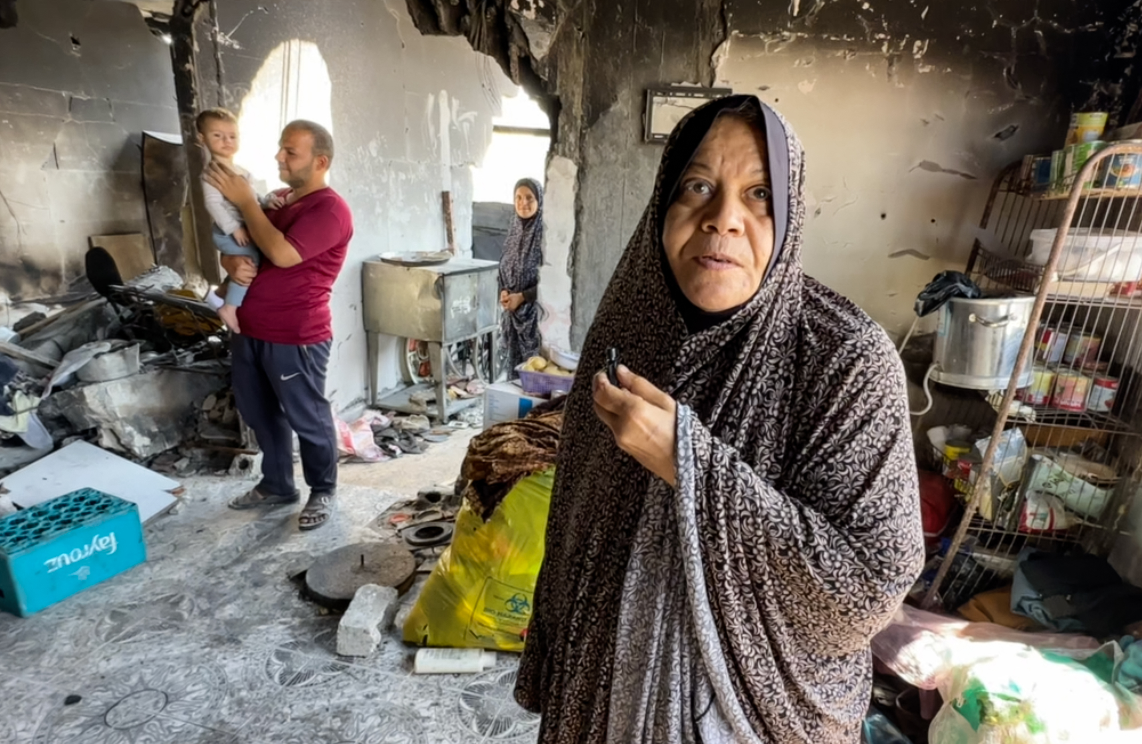 Woman in flowered isdal speaks, family members in the background among what remeans of the home